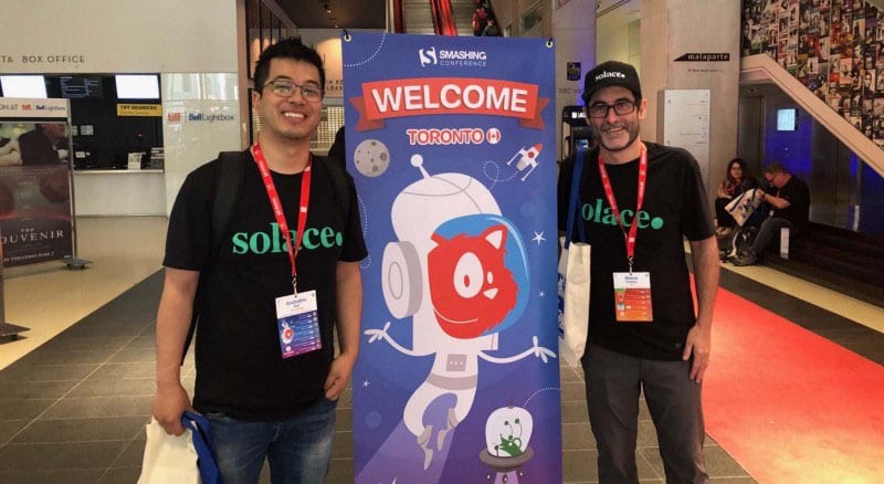 A photo of Arshabhi Rai and Blaine Hussey standing in front of the SmashingConf Toronto 2019 welcome poster